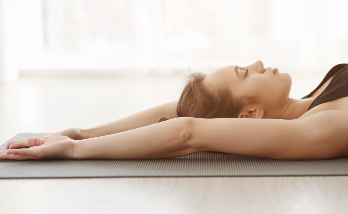 Relaxed yoga girl laying on mat, doing breathing exercise, panorama, side view